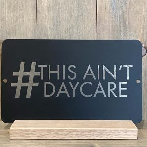 this aint daycare black license plate metal wall hanging on a wood shelf