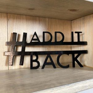 close up of shelf with metal hashtag sign on it, sign says "add it back"